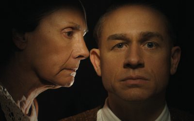 A cinematic image of an older woman on the verge of whispering something into a younger man's ear.